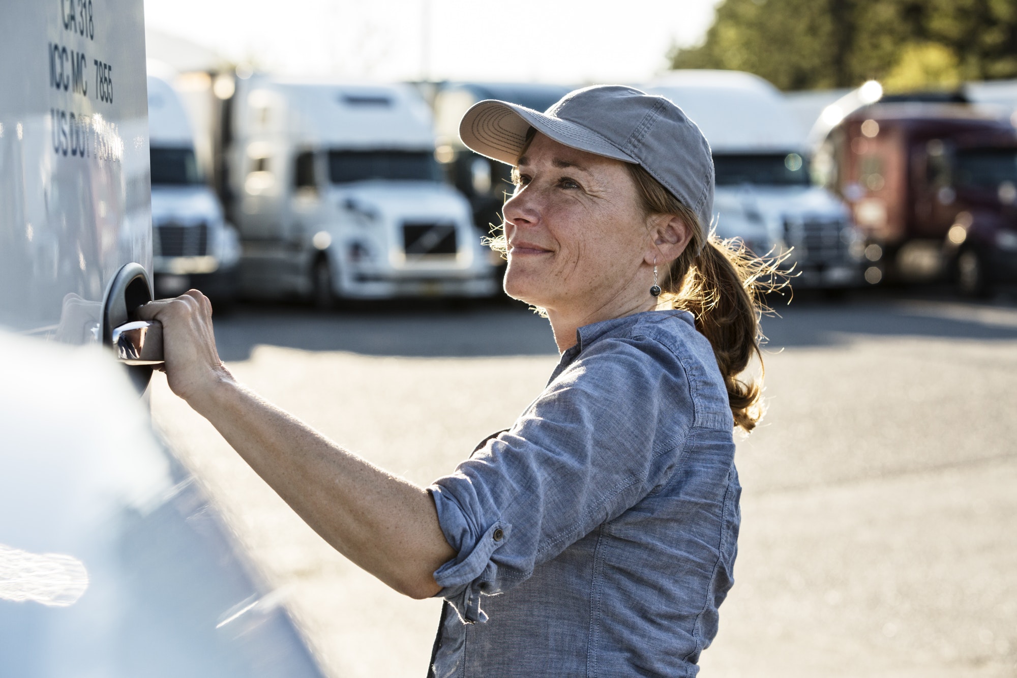 Caucasan female truck driver getting into her truck parked in a lot at a truck stop.